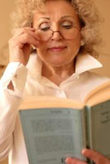 presbyoipa older woman using reading glasses to read a book.